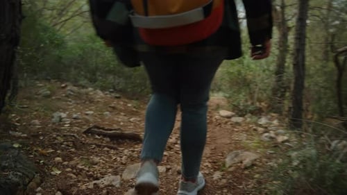 Following Behind a Sporty Woman Descending from the Mountain on a Rocky Steep Path with a Backpack