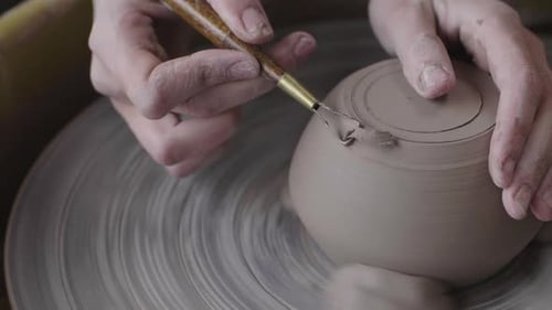 Une personne sculptant de l'argile dans une tasse sur un tour de potier.