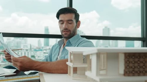 Man Reviews Blueprints at Desk in City Office