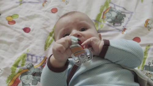 Infant Chewing on Toy Lying on Bedding