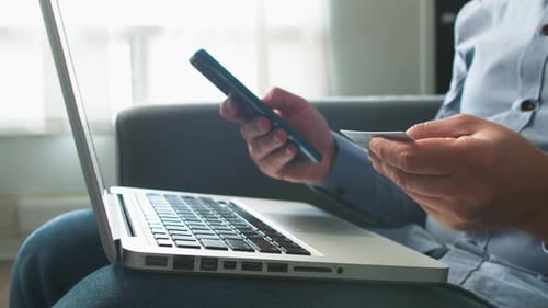 Person Uses Phone and Card with Laptop