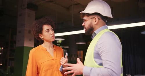 Male Project Manager Discussing Building Plan with Female Engineer in Hard Hat and Safety Vest