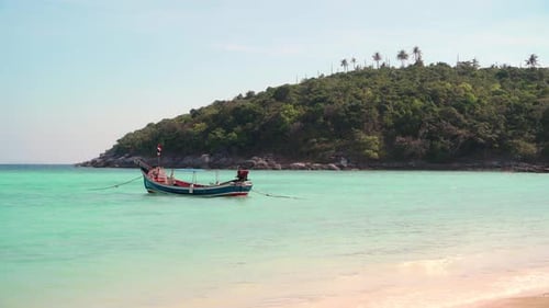 A Thai traditional longtail tourist boat bobs on turquoise transparent waves.