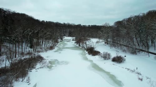 Drone view of frozen creek surrounded by forest in winter