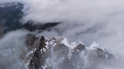 Aerial View of Snowy Mountain Peak with Rolling Clouds and Mist