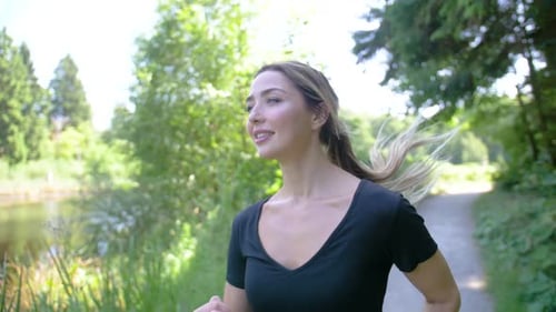 A pretty woman jogging in a park, smiling and enjoying the scenery as she runs. Slow motion, close u