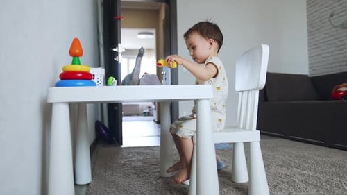 Sweet Caucasian baby boy sits at the desk. Cute toddler plays with toy animals. Low angle view.