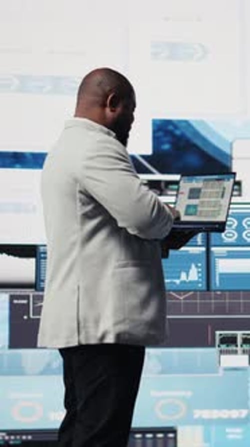 Man Using Laptop in Front of Data Monitors