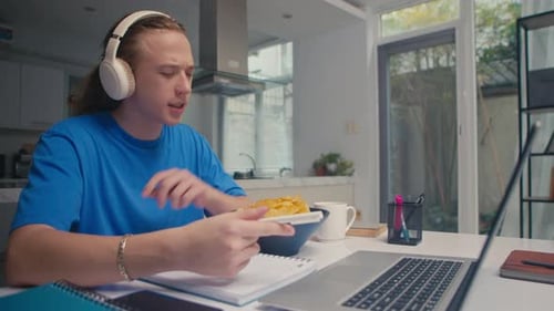 Young Adult Studying and Eating Chips at Home