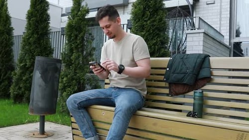 Man Sitting on Bench Using Smartphone in Urban Park