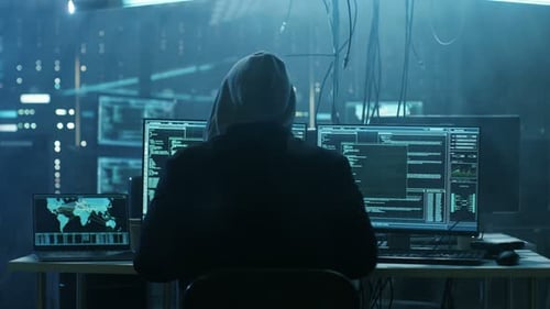 Hooded Hacker Working on Computers in a Dark Office