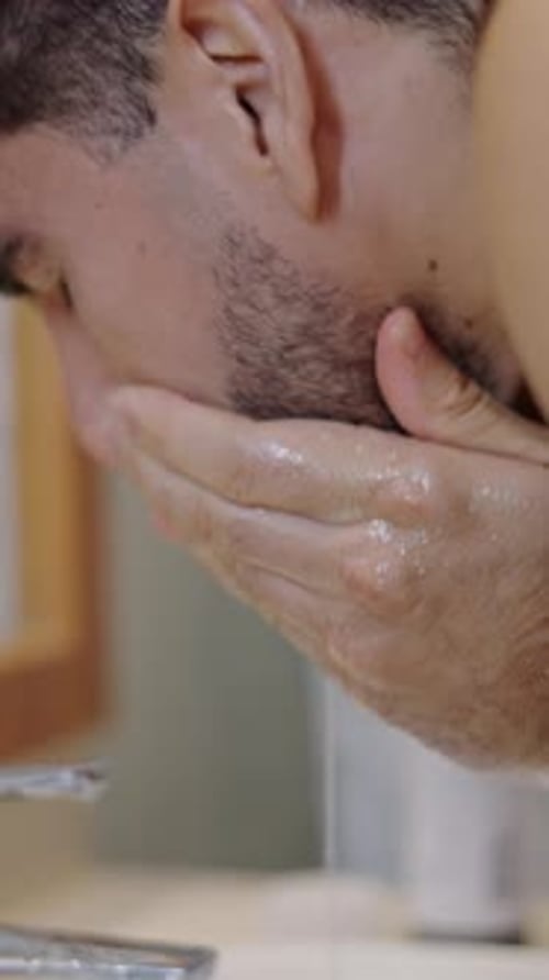 Hombre barbudo se lava la cara después de afeitarse