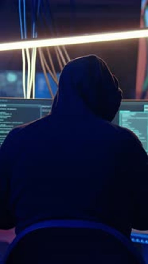 Person in Hoodie Working at Computers at Night