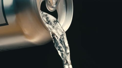 Vino blanco o líquido transparente que sale de una lata de plata en cámara lenta, fondo negro de caña
