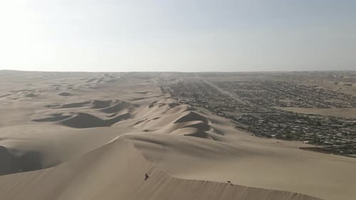 Aerial: Tourists hike up massive desert sand dune in arid Ica Peru