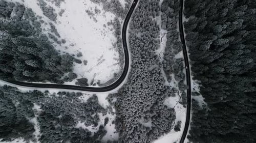 A Picturesque Aerial View Showcasing a Winding Road That Traverses Through a Snowy Forest Landscape