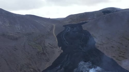 Black basalt river flows into valley along slope of Iceland highlands