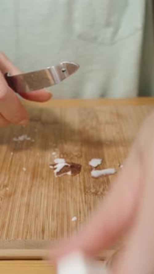 Vertical video. A Woman Takes Coconut Pieces from the Plate and Peels the Skin Off Them.