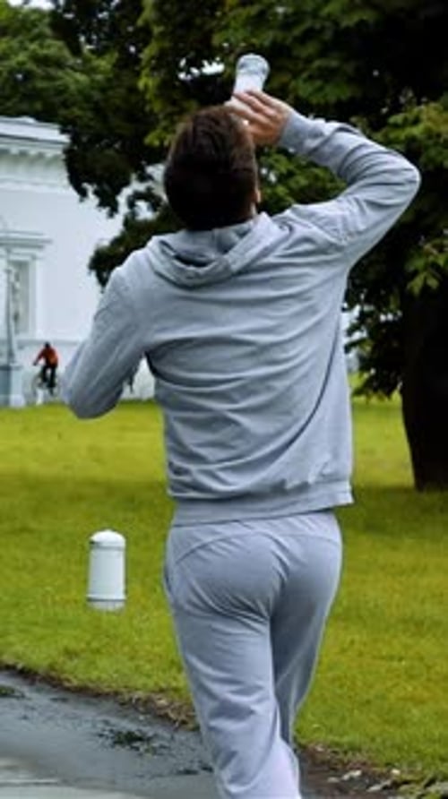 Man Runs with Water Bottle on Head in Park