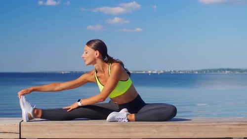 Woman Stretching on Dock by Water on a Sunny Day