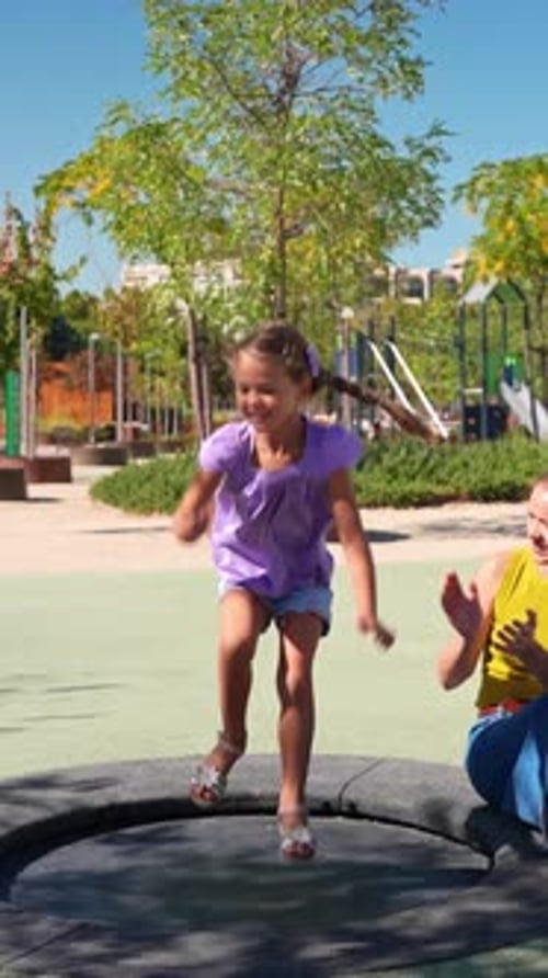 Happy Little Girl Jumping on Trampoline at Playground