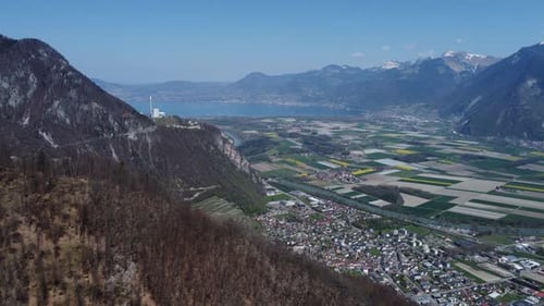Slow expansive aerial shot of a farmland valley in Switzerland with Lake Geneva in the background.