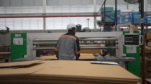 Industrial Worker Cutting Corrugated Cardboard Sheet in Factory