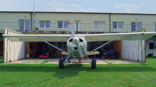 Kleines Flugzeug, das den Hangar verlässt und vom professionellen Piloten Sunny Day gesteuert wird. Weißes Flugzeug