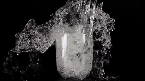 A jet of water is poured into glass goblets on a black background and creates a splash of water