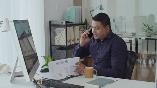 Man Talking on Phone While Reviewing Documents at Desk