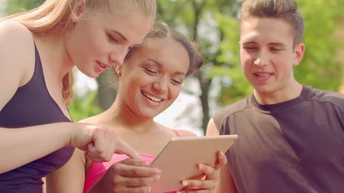 Young people enjoying tablet technology together in sunny outdoor park
