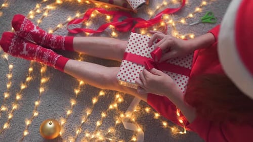 Woman Wrapping Christmas Present with Ribbon on Floor