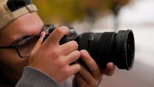 Close up of young male photographer raises up professional camera to take a photo