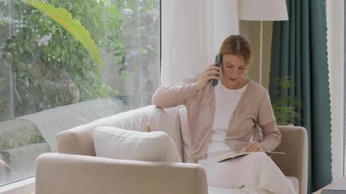 Freelance Female Manager Talking on Phone and Taking Notes at Home Office