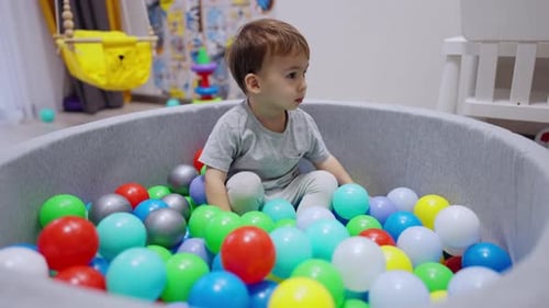 Un petit garçon calme est assis dans les boules dans une piscine sèche.