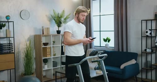 Man Using Phone Near Treadmill at Home