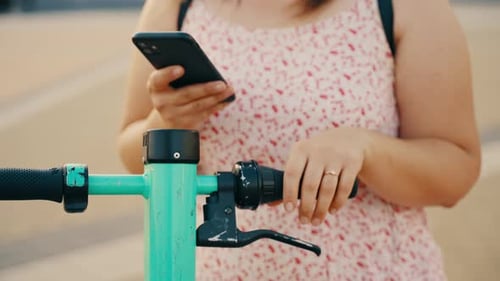Woman Uses Smart Phone Next to Electric Scooter