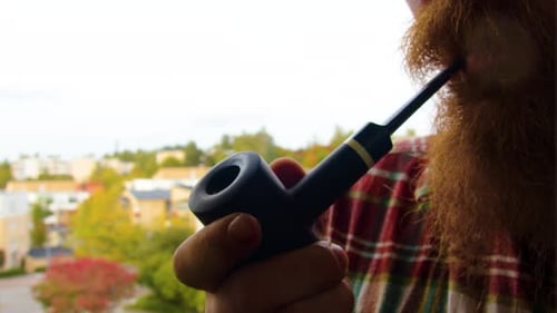 Nahaufnahme eines modernen Mannes mit Ingwerbart, der eine antike Vintage-Pfeife in dunkelschwarzer Farbe in seinem Ha hält