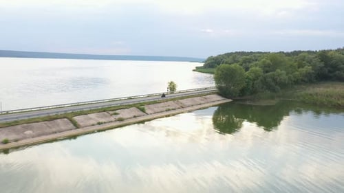 Aerial Shot of Motorcyclist Racing His Motorcycle Through Road Near Lake Man Drive Bike at Dam Route