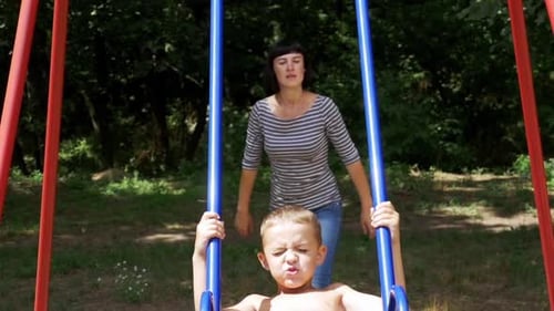 Mother Swinging Her Happy Child Boy on a Street Swing at Playground in Slow Motion