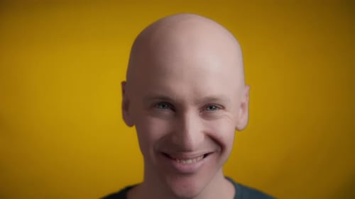 Bald Man Smiling in Front of Yellow Backdrop