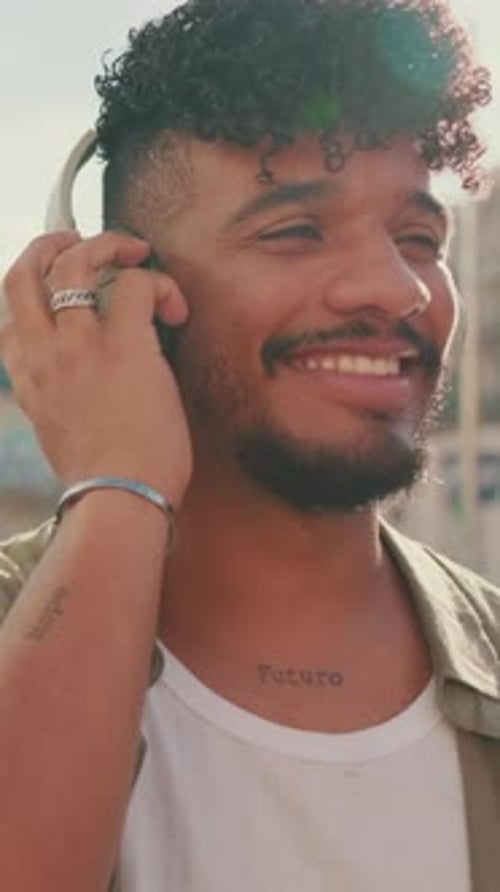 Close up, young man with beard in an olive-colored shirt listens to music on headphones, dances
