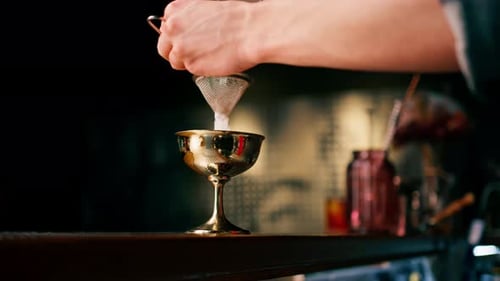 Bartender Pouring Cocktail Through Strainer into Glass