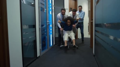 Multiracial Colleagues Having Fun Racing Office Chair in Corporate Building. Entrepreneur Team