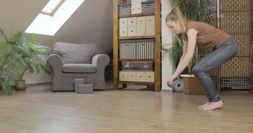 Young blonde woman rolls out her yoga mat in her home studio.