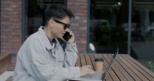 Young Adult Uses Laptop and Phone Outdoors
