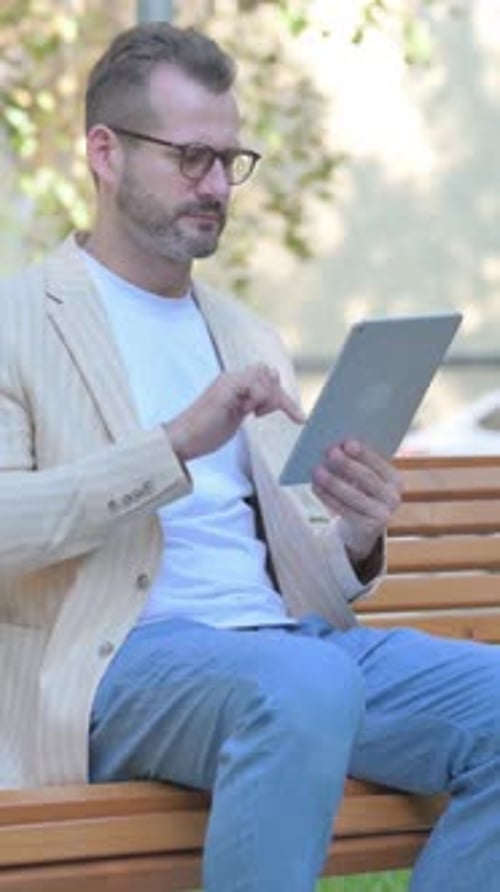 Man Sitting on Bench Using Tablet in Park