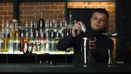 A bartender adding salt to the shaker with alcoholic cocktail at the bar or disco club