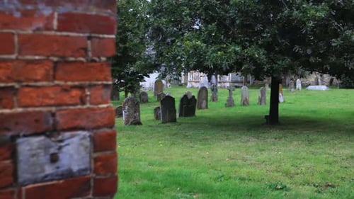 Walking into old graveyard with mossy headstones coming from outside wall. Daytime, overcast.