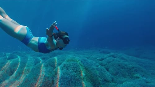 Woman swims underwater in the tropical sea and slowly moves over the sea bottom